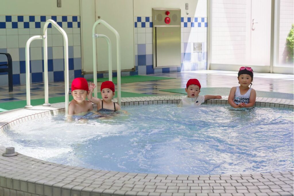 円形の浅い子ども用プールに肩まで浸かって並ぶ幼い子どもたち