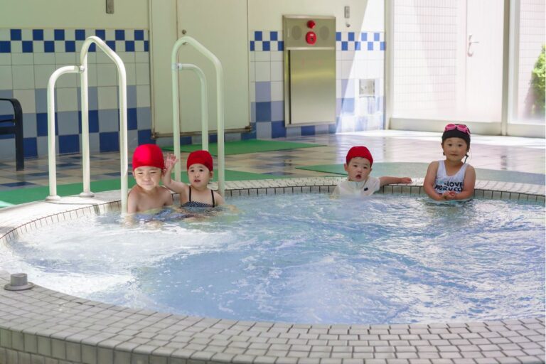 円形の浅い子ども用プールに肩まで浸かって並ぶ幼い子どもたち