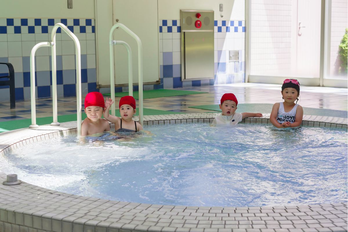 円形の浅い子ども用プールに肩まで浸かって並ぶ幼い子どもたち