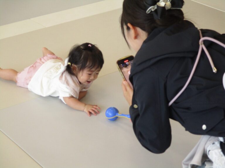 マットの上でうつ伏せになった赤ちゃんと、写真を撮る大人