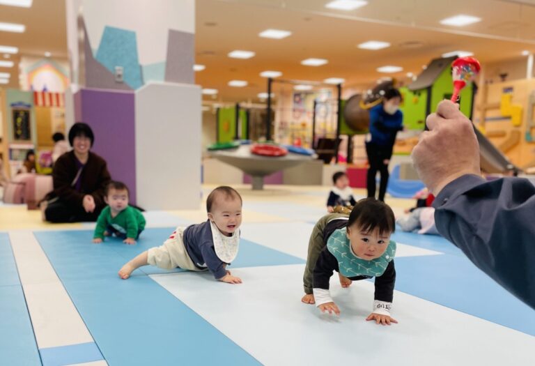 マットの上でハイハイをする赤ちゃんたちと、見守る大人