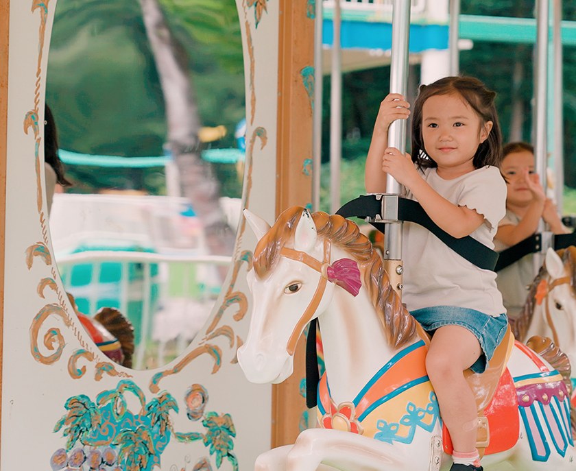 メリーゴーランドの木馬にベルトで固定されて乗る幼い子ども