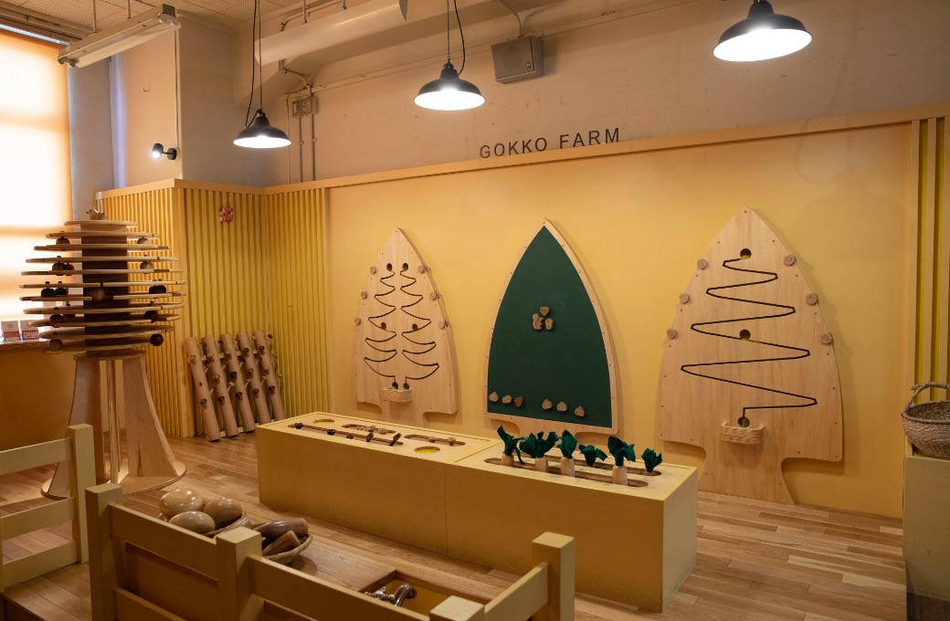 黄色い壁のGOKKO FARMコーナーに木製の果物や野菜のおもちゃが並ぶ「おもちゃのまち きいろ」
