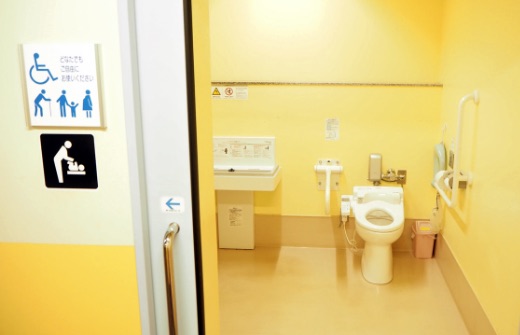 手すり付き便器と手洗いがある、黄色い壁の「だれでもトイレ」の内部