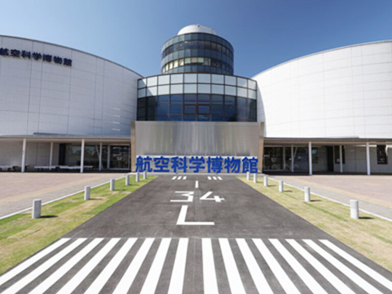 滑走路に見立てた白線の通路の先に建つ、円筒形の塔をもつ博物館の建物