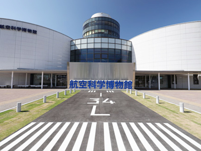 滑走路に見立てた白線の通路の先に建つ、円筒形の塔をもつ博物館の建物