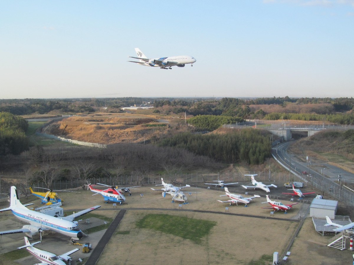 上空から見た屋外展示場。小型機が並び、奥を旅客機が飛んでいる