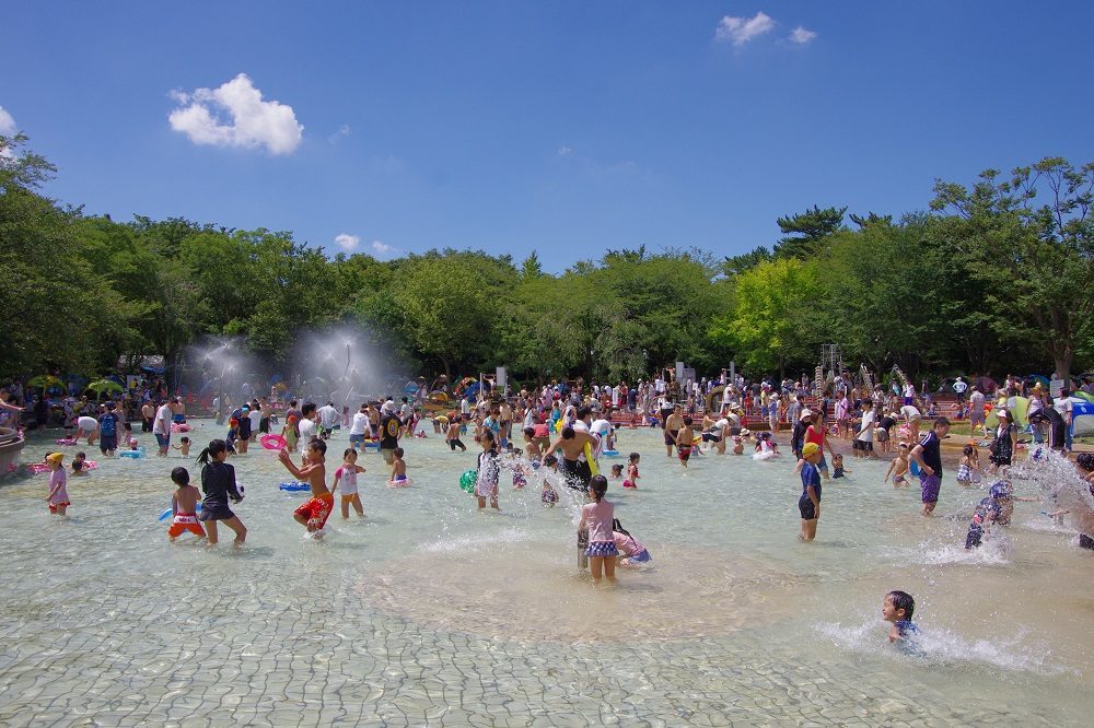 浅い池で水遊びをする大勢の子どもたち。奥から霧状の水が噴き出している