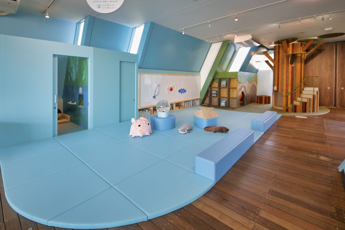 水色のマットが敷かれ、ぬいぐるみと低い棚が置かれた子ども向けの広場