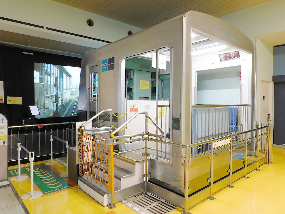 実物大の運転台が入った箱型のブース。手前に3段の階段と手すりがあり、左の壁に走行映像を映す大きなスクリーンがある
