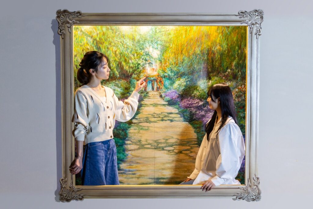 壁に掛かった大きな額縁の中の風景画に、2人が入り込んで立っているトリックアート
