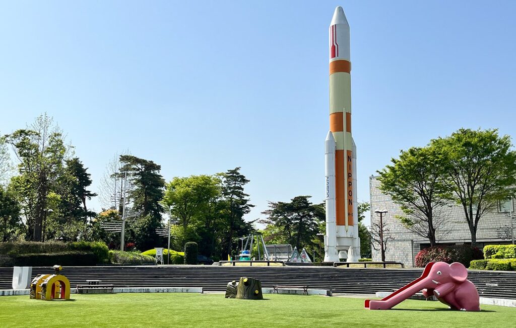 芝生の広場の奥に、白とオレンジの大きなロケットの模型が立っている