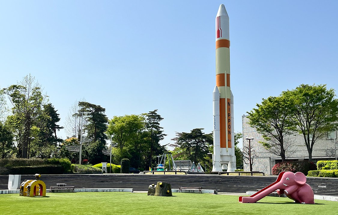 芝生の広場の奥に、白とオレンジの大きなロケットの模型が立っている
