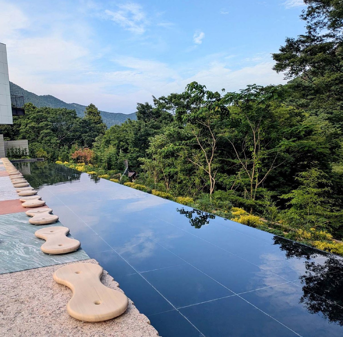 細長い足湯が奥までまっすぐ伸び、縁に木の腰かけが並ぶ。奥に箱根の山なみと青空
