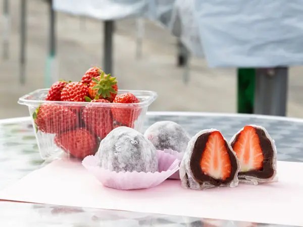 丸いテーブルに、いちごのパックと、粉をまぶした大福、断面にいちごが入った大福が並んでいる