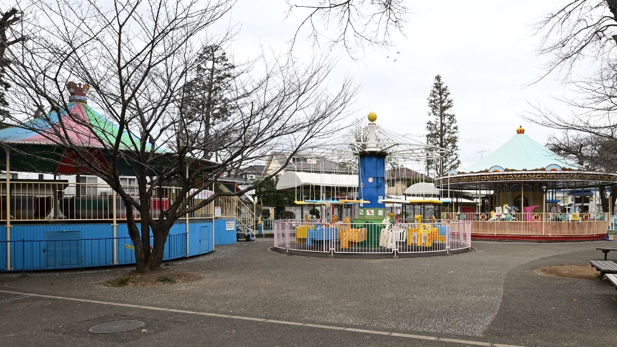 メリーゴーラウンドなどの乗り物が並ぶ屋外のミニ遊園地