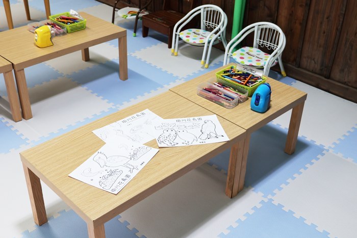 マット敷きの床に低い机と子ども用の椅子が並ぶぬり絵コーナー