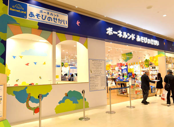 ショッピングモールの中にある店の入口。青い看板に「ボーネルンド あそびのせかい」と書かれ、左手に木と鳥を描いた白い壁、右手におもちゃの売り場が見える