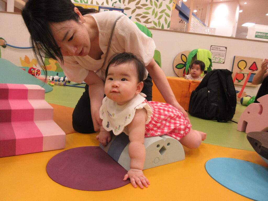 やわらかい遊具に手をついた赤ちゃんを、うしろから大人が支えている