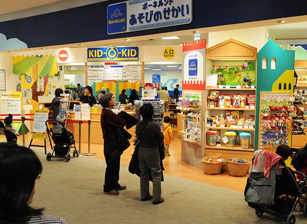 店の入口と受付カウンター。「KID-O-KID」の看板と「入口 ENTER」の表示があり、右手におもちゃの棚、左手にベビーカー置き場が見える