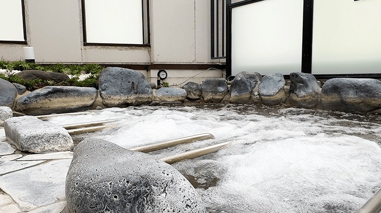 岩で縁取られた浴槽。湯面が白く泡立ち、石の枕が並んでいる