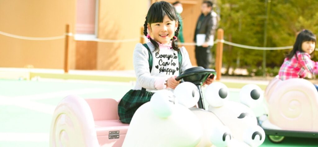カタツムリの形をした白い乗り物のハンドルを握る子ども。うしろにピンクの座席がついている