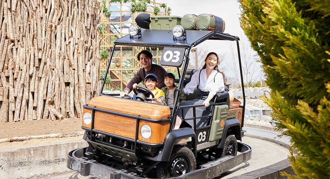 木目のボディの小さなオフロード車に、大人2人と子ども2人が乗って未舗装のコースを走っている
