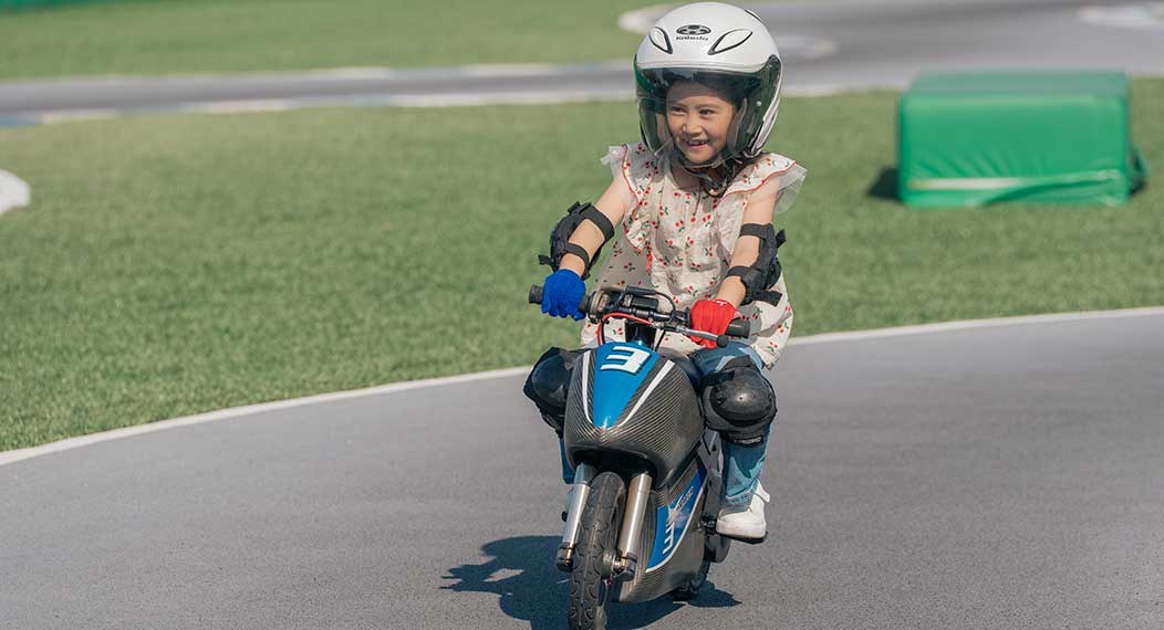 ヘルメットとプロテクターをつけた子どもが、小さなバイクに乗って舗装されたコースを走っている