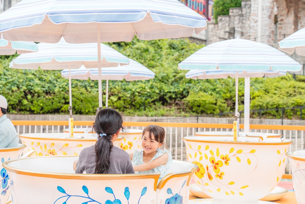 花模様の白いカップにパラソルが立つティーカップの乗り場。カップの中で子どもと大人が向かい合っている