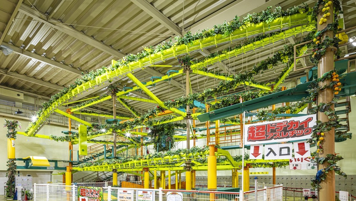 天井近くまで緑の通路が組まれた屋内アスレチックと入口の看板