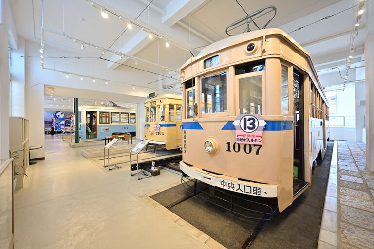 白い床の広い屋内展示室に、クリーム色と青の市電が線路ごと並んでいる