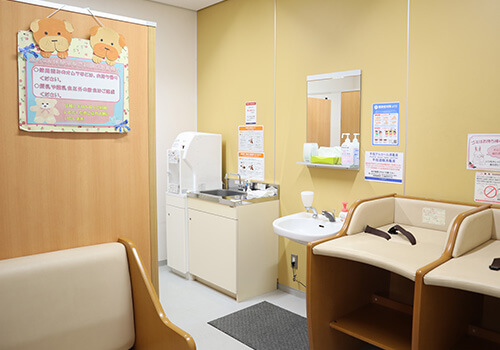 赤ちゃん休憩室の室内。流し台の上に給湯器があり、右手におむつ替え台が2台、左手にソファが置かれている