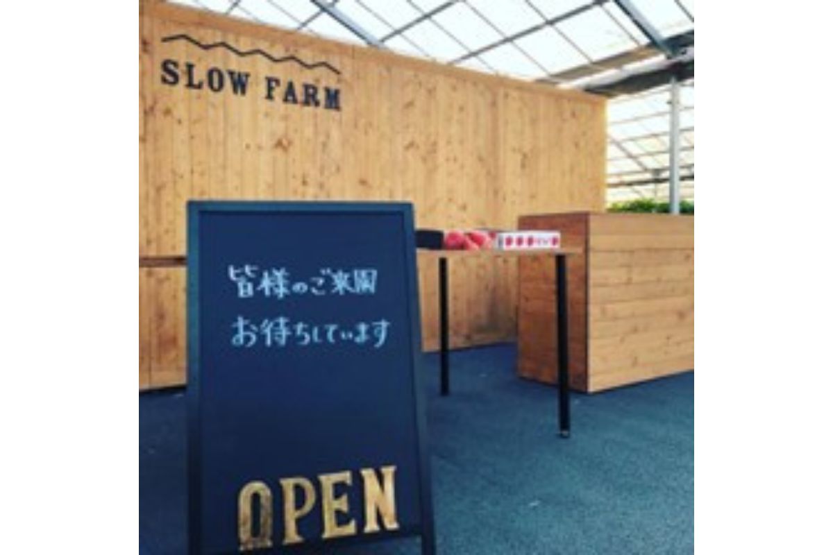 木づくりの受付カウンター。上に「SLOW FARM」の木の看板があり、手前に「皆様のご来園お待ちしています OPEN」と書かれた黒板が立っている