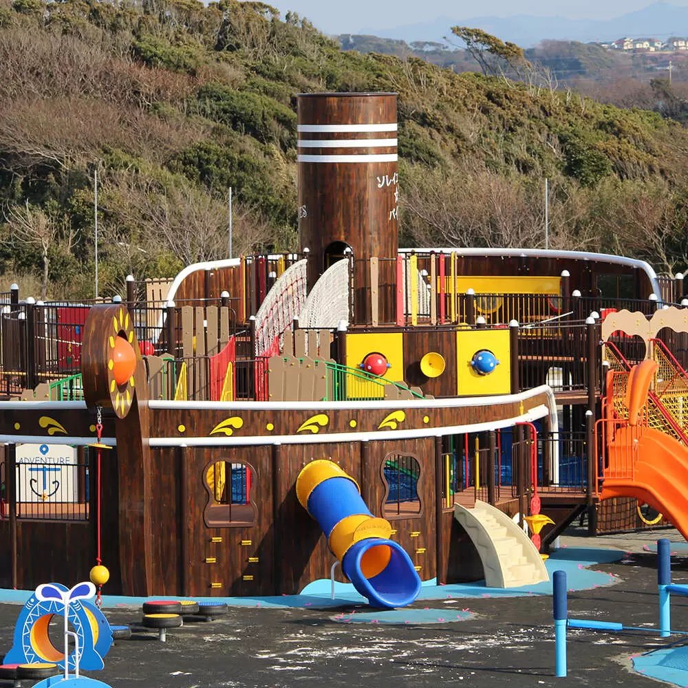 海賊船の形をした大きな木製の複合遊具。青と黄色のすべり台が2本ついている