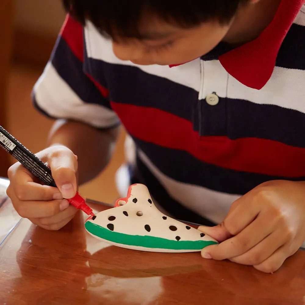 机に向かった子どもが、白い陶器の小物にペンで模様を描いている