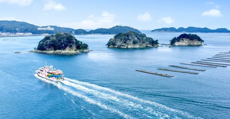 青い海に並ぶ3つの小島と、その手前を走る白い遊覧船