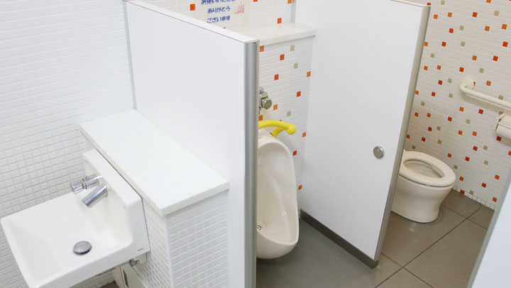 低い位置に取り付けられた小さな手洗いと小便器、子どもの背丈に合わせた個室のトイレ