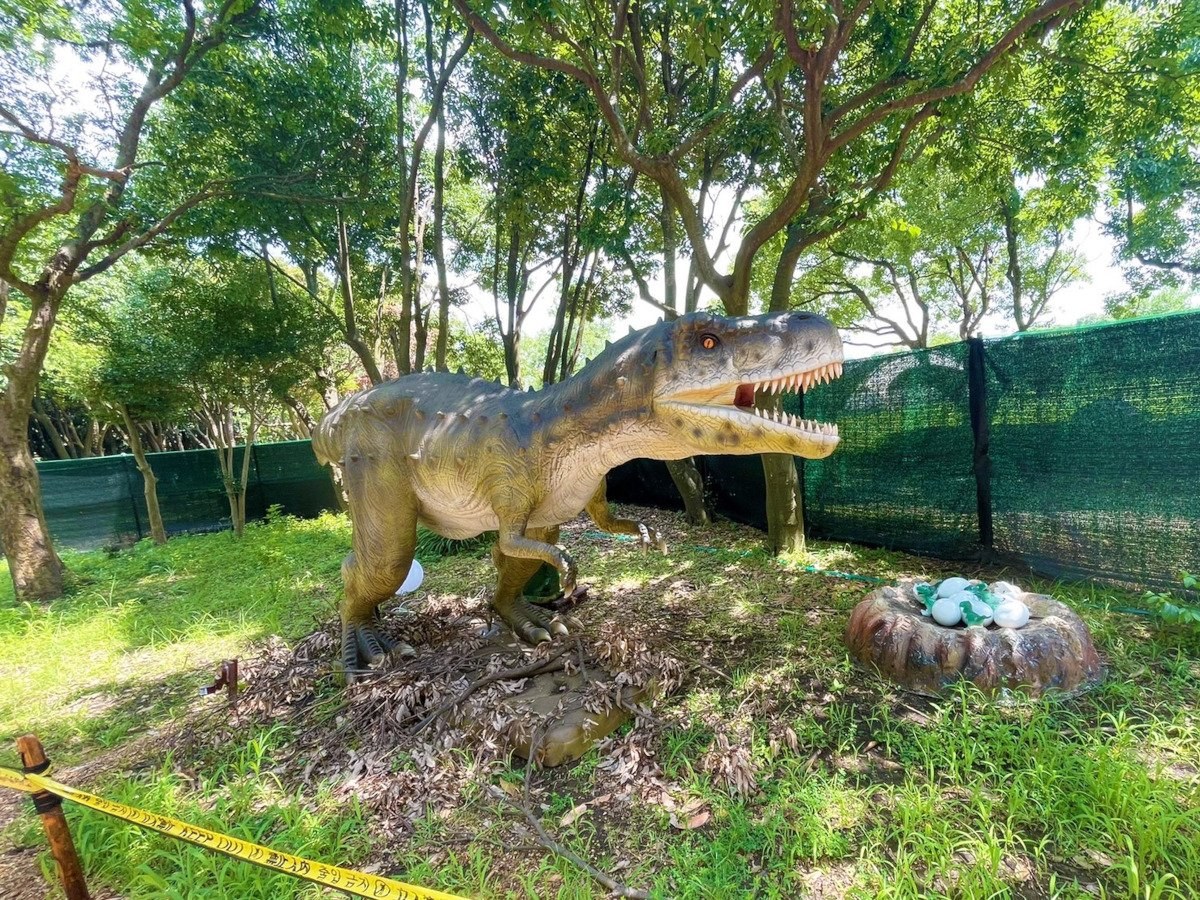 木立の中に立つティラノサウルスの模型と卵の巣