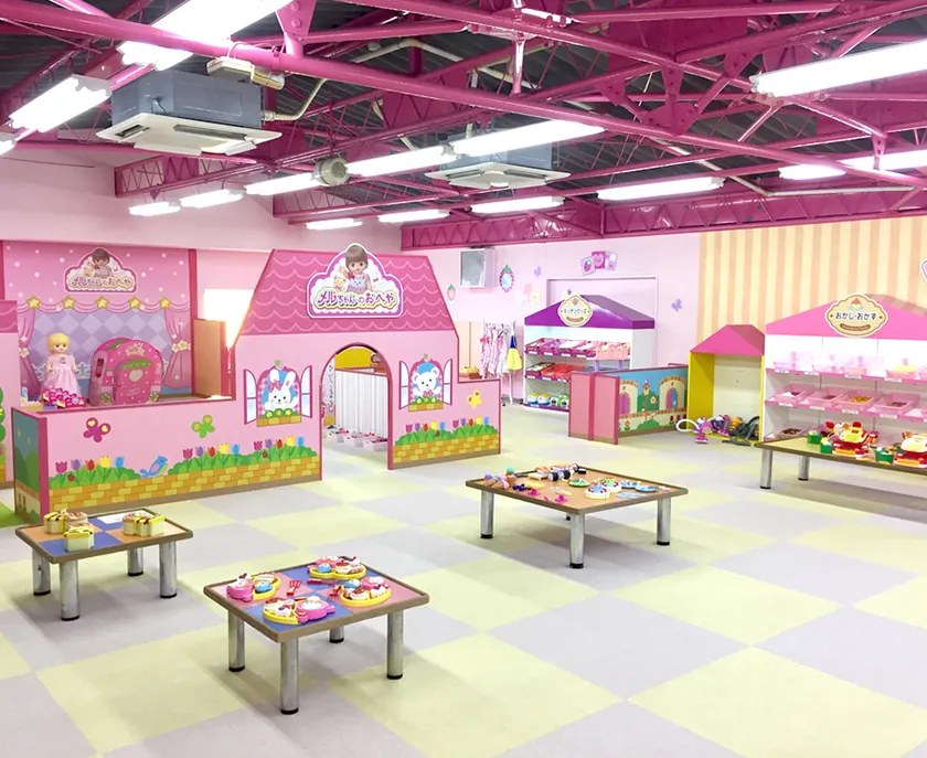 マットを敷いた床に低いテーブルが並び、奥にメルちゃんのおへやの看板があるピンクの部屋