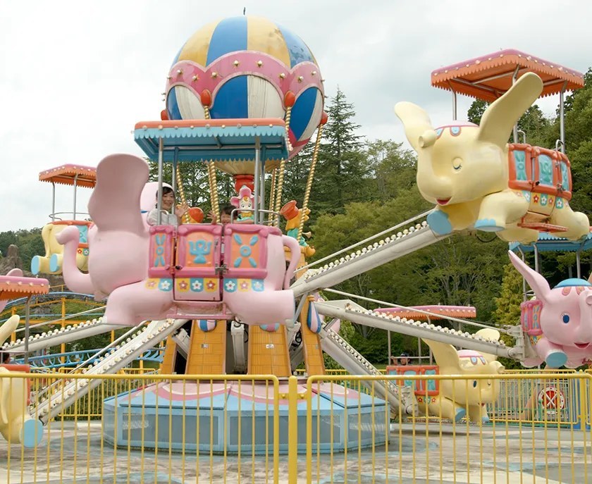 気球の飾りを中心に、ピンクと黄色のゾウの乗り物が腕の先で回る遊具